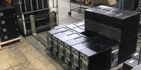 Stacked black computer servers in a warehouse setting, showcasing equipment ready for inventory management and potential deployment.