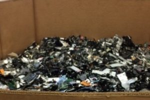 Box filled with electronic waste, including shattered circuit boards and components, highlighting the issue of e-waste recycling.