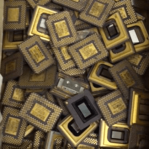 A collection of computer microprocessors scattered in a box, showcasing their intricate designs and gold contacts, relevant for discussions on technology or electronics recycling.