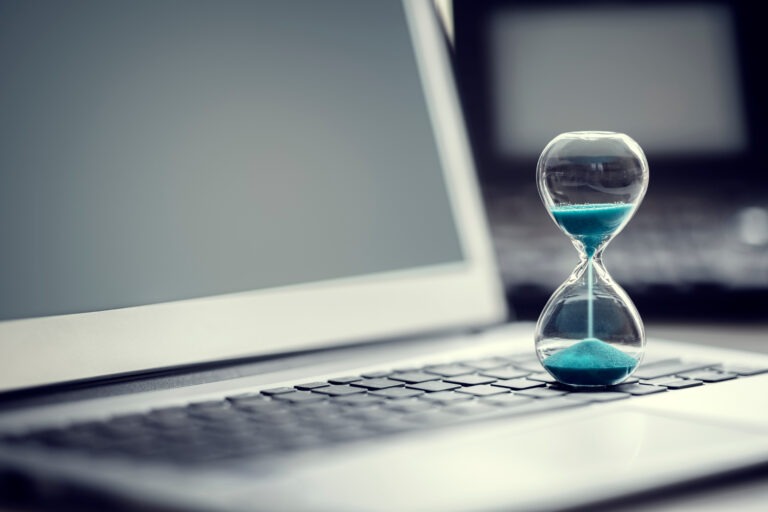 Hourglass with blue sand resting on a laptop keyboard, symbolizing time management and productivity in a digital workspace.